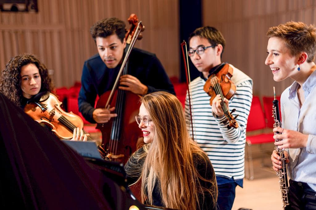 String students look over the shoulder of a piano accompanist